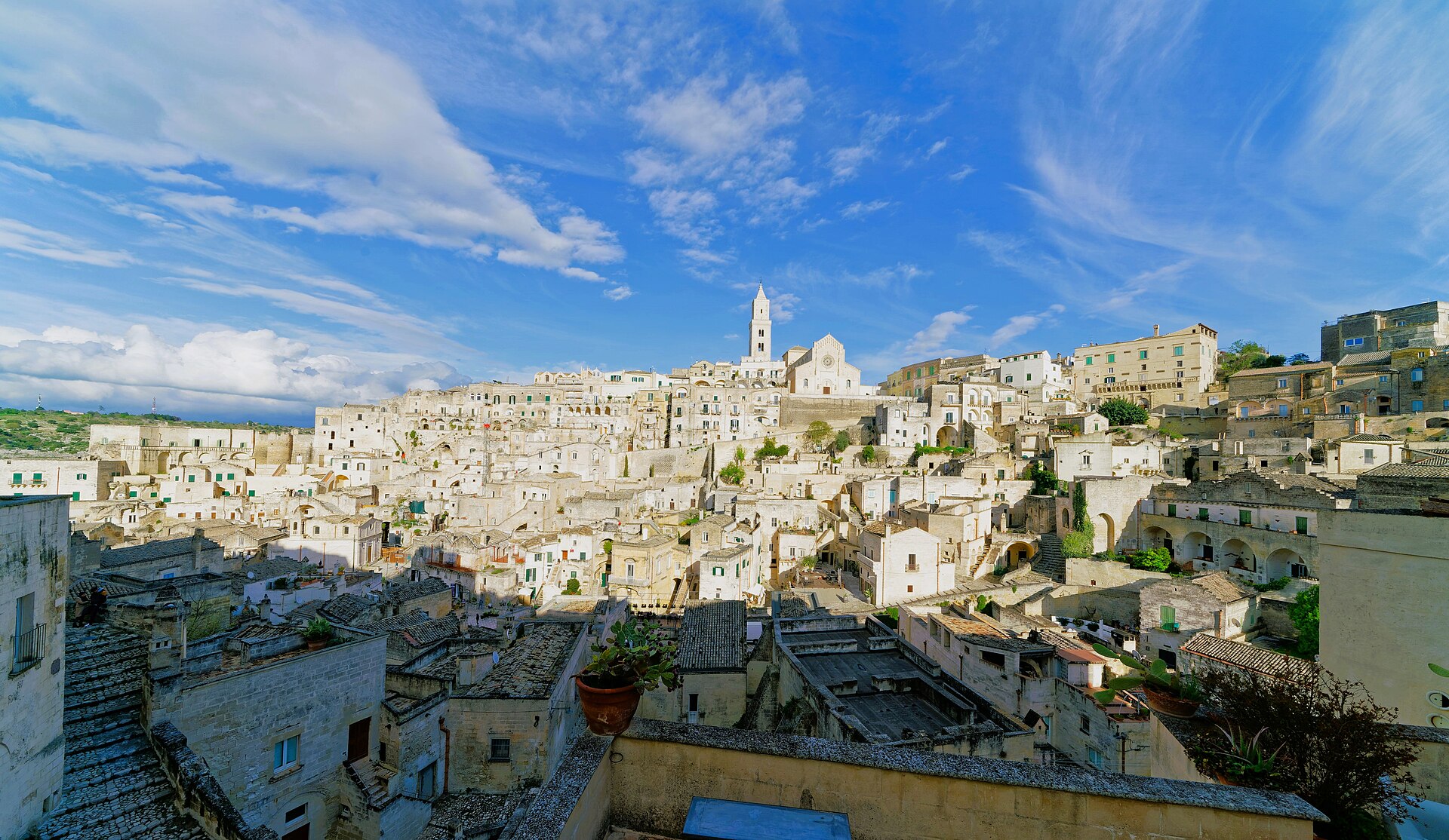 Panorama dei Sassi di Matera con la cattedrale sul poggio, tetti in pietra e cielo con nuvole.